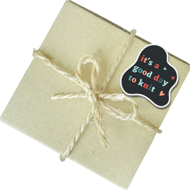 May include: A brown paper package tied with twine and a black sticker that says "it's a good day to knit" with red, pink, and teal lettering and small hearts.