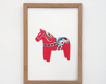 May include: A framed print featuring a red Dala horse, a traditional Swedish wooden figurine. The horse is decorated with white, blue, and yellow floral patterns. The frame is made of light-colored wood, and the background is white.
