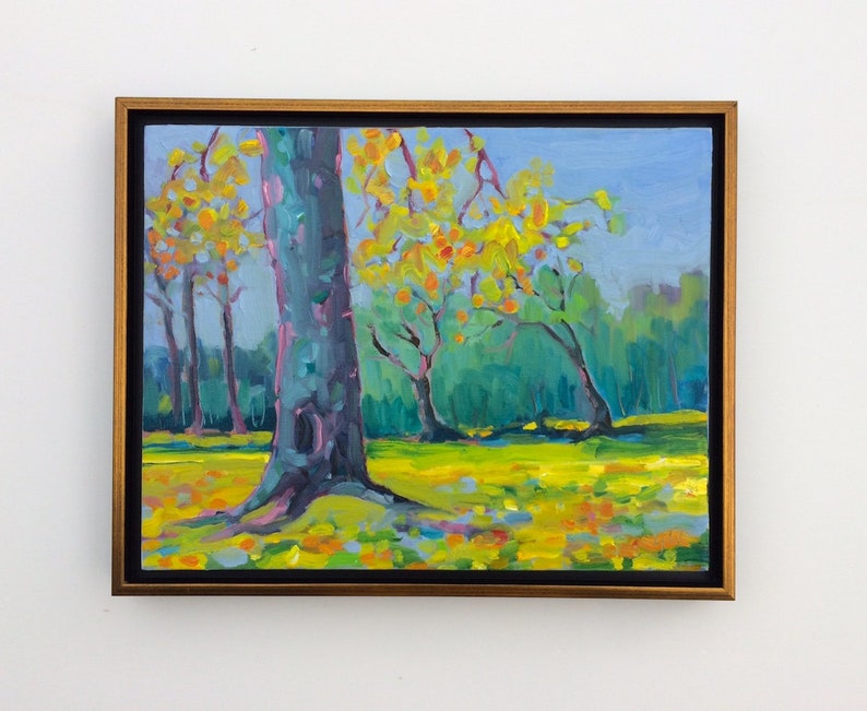 Puede incluir: Pintura al &oacute;leo de una escena de parque con &aacute;rboles y una zona de c&eacute;sped. Los &aacute;rboles tienen hojas amarillas y naranjas, y la hierba es de un verde-amarillo vibrante. El cielo es azul claro y la pintura est&aacute; enmarcada en un marco dorado.
