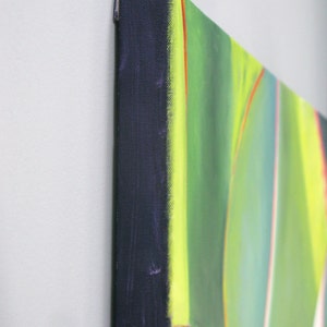 May include: Close-up of a canvas art piece with a vibrant abstract design. The artwork features a palette of green, yellow, and red hues. The canvas edges are wrapped in a dark blue fabric, creating a clean, finished look.