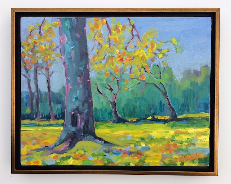 Puede incluir: Una pintura al &oacute;leo de un paisaje con &aacute;rboles de hojas amarillas y naranjas, sobre un fondo de follaje verde y cielo azul. La obra de arte est&aacute; enmarcada en un marco dorado con un borde interior negro, creando una pieza vibrante y colorida.