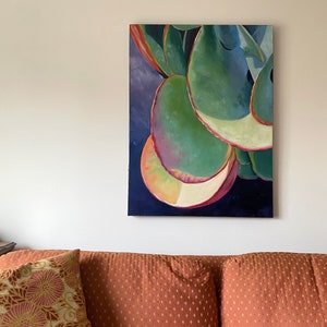 May include: An abstract painting of a succulent plant with large, rounded green leaves. The leaves have red and yellow edges, set against a dark blue background. The artwork hangs above a rust-colored couch with patterned pillows.