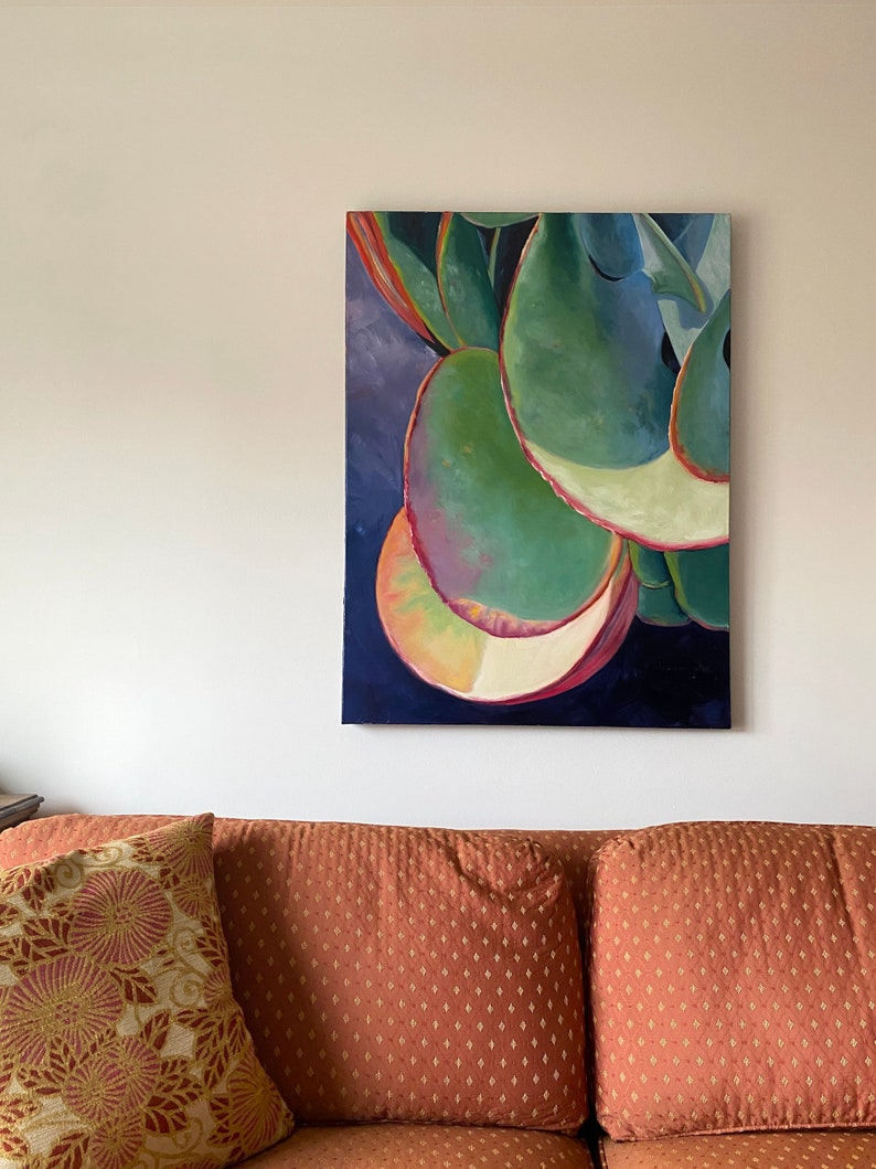 May include: An abstract painting of a succulent plant with large, rounded green leaves. The leaves have red and yellow edges, set against a dark blue background. The artwork hangs above a rust-colored couch with patterned pillows.