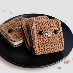 Könnte beinhalten: Drei gehäkelte Schokoladenkekse auf einem schwarzen Teller. Die Kekse haben ein lächelndes Gesicht und sind mit weißem Zuckerguss verziert. Der Text "chocolate Cooies crochet gift ideas Food Crafts Easy crochet かぎ針編み!" ist im Hintergrund.
