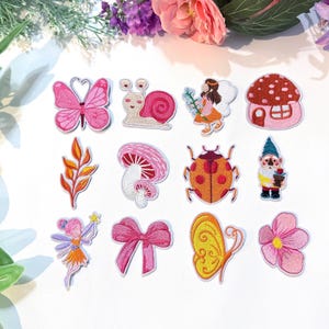 May include: A collection of embroidered patches featuring whimsical designs. Includes a pink butterfly, a snail, a fairy, a mushroom house, a leaf, a mushroom, a ladybug, a gnome, a fairy with a wand, a pink bow, a yellow butterfly, and a pink flower.