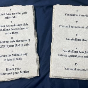 May include: Two stone plaques with the Ten Commandments engraved in black text. The plaques are light gray with a rough texture. The first plaque has the first five commandments, and the second plaque has the last five commandments.