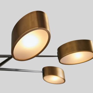 May include: A modern, multi-light chandelier with a black metal frame and gold-toned, oval-shaped light fixtures. The light fixtures have frosted glass diffusers.