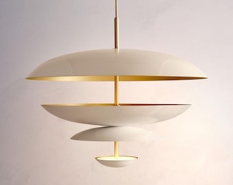 May include: A multi-tiered pendant light fixture featuring four stacked, saucer-shaped shades in a matte off-white finish. The interior surfaces of the shades are gold-toned, and they are connected by a central vertical rod in a polished gold finish.