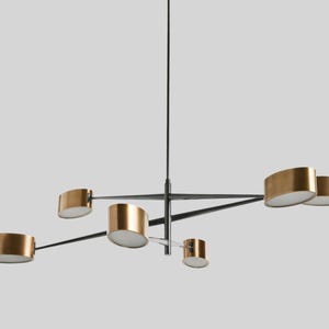 May include: A modern, black metal chandelier with five gold-toned, oval-shaped light fixtures. The fixtures are suspended from a central rod and extend outwards on arms.