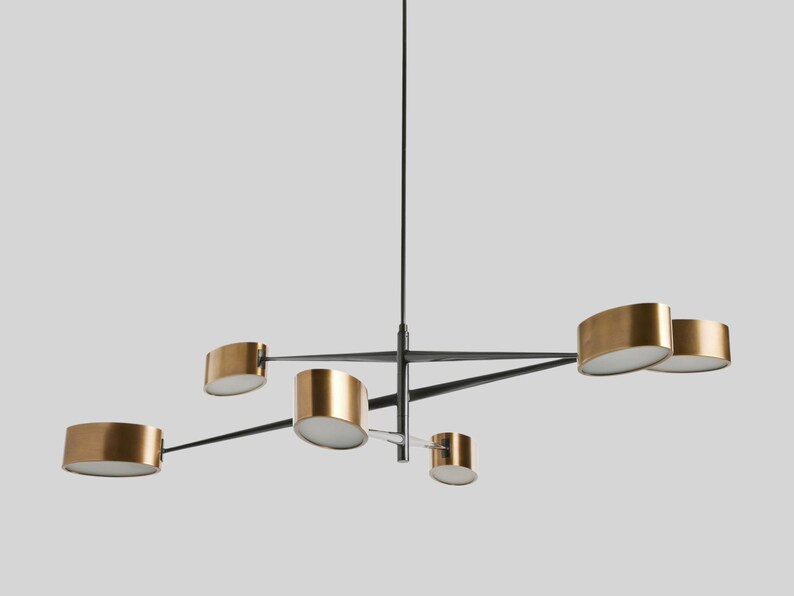 May include: A modern, black metal chandelier with five gold-toned, oval-shaped light fixtures. The fixtures are suspended from a central rod and extend outwards on arms.