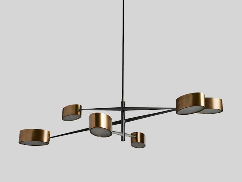 May include: A modern chandelier with five gold-toned light fixtures and black metal arms. The chandelier has a minimalist design and is suspended from a single black cord.