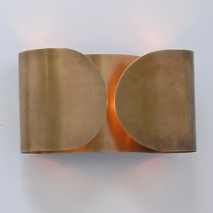 May include: A brass wall sconce with a unique design. The sconce features a curved, semi-circular shape with a warm, golden hue. The light source is visible in the center, creating a soft glow. This fixture is ideal for adding a touch of elegance to any space.