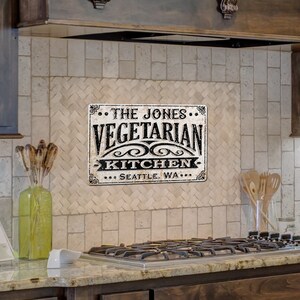 May include: A black and white metal sign with the text "The Jones Vegetarian Kitchen... Seattle, WA..." on a white tiled kitchen backsplash.