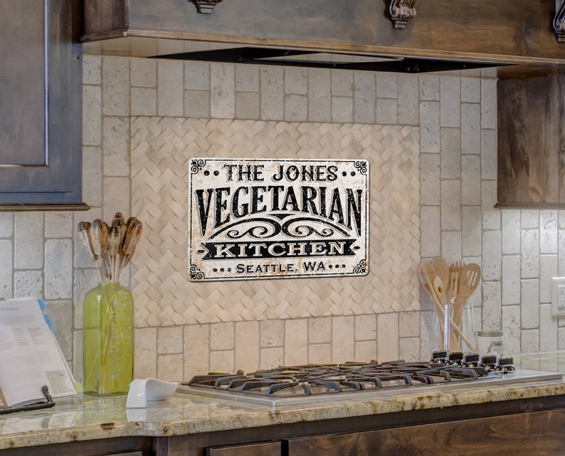 May include: A black and white metal sign with the text "The Jones Vegetarian Kitchen... Seattle, WA..." on a white tiled kitchen backsplash.