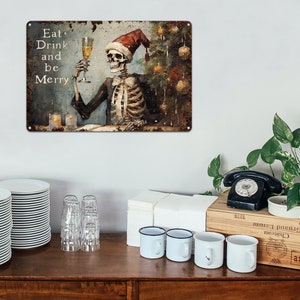 May include: A metal sign with a distressed, rusty look featuring a skeleton wearing a Santa hat and holding a glass of champagne. The sign reads "Eat, Drink and be Merry".