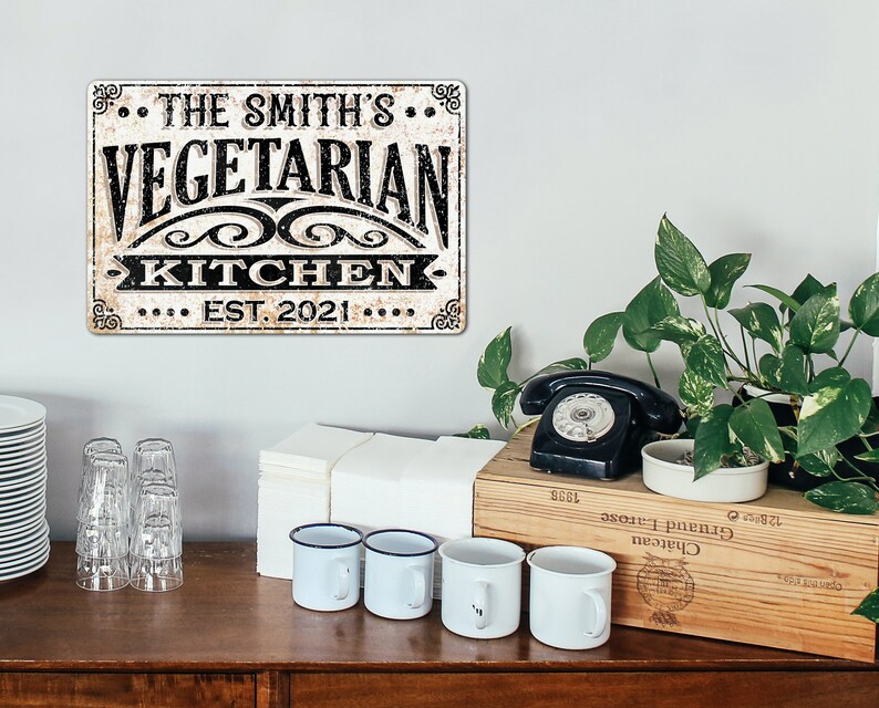May include: A vintage-style metal sign with a distressed white background and black text. The sign reads "The Smith's Vegetarian Kitchen Est. 2021".
