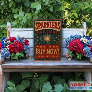 K&ouml;nnte beinhalten: Ein Vintage-Schild aus Metall in den Farben Rot, Wei&szlig; und Blau. Es tr&auml;gt die Aufschrift "Sparkler Brilliant Buy Now!" und zeigt eine Feuerwerks-Illustration. Das Schild ist auf einer Holzbank mit roten, wei&szlig;en und blauen Blumen platziert.