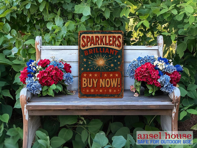 K&ouml;nnte beinhalten: Ein Vintage-Schild aus Metall in den Farben Rot, Wei&szlig; und Blau. Es tr&auml;gt die Aufschrift "Sparkler Brilliant Buy Now!" und zeigt eine Feuerwerks-Illustration. Das Schild ist auf einer Holzbank mit roten, wei&szlig;en und blauen Blumen platziert.