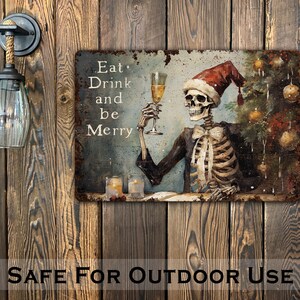 May include: A metal sign with a distressed, rusty look featuring a skeleton wearing a Santa hat and holding a glass of champagne. The sign reads "Eat, Drink and be Merry".