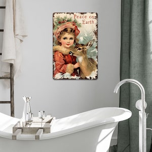 Puede incluir: Un letrero de metal vintage con tem&aacute;tica navide&ntilde;a que presenta a una ni&ntilde;a con un vestido rojo y un sombrero blanco sosteniendo un cervatillo. El letrero tiene un aspecto desgastado y dice "Peace on Earth".