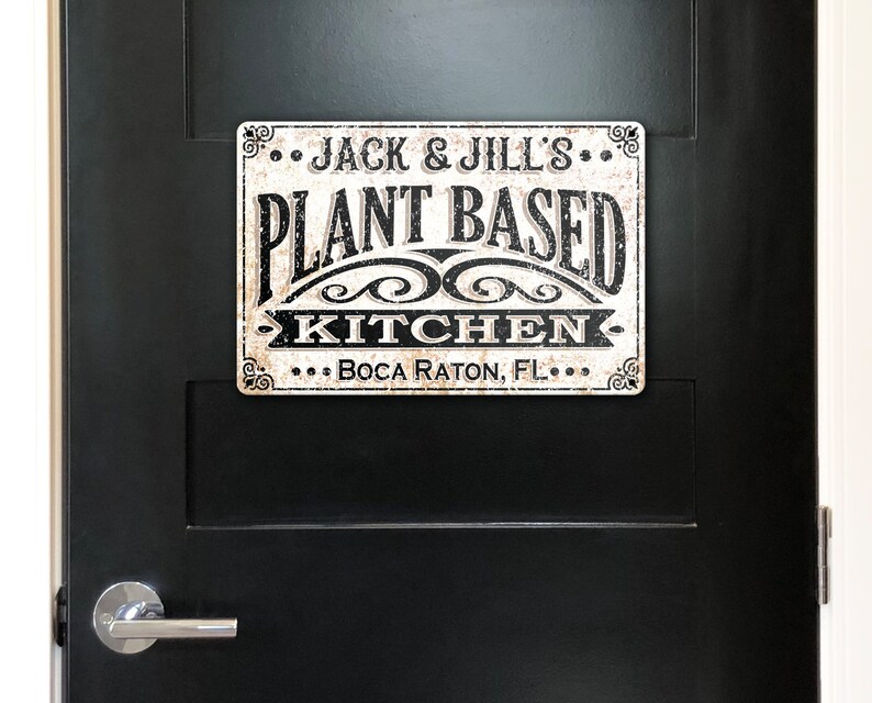 Op de afbeelding: Een wit bord met zwarte tekst dat "...Jack & Jill's... Plantaardige keuken... Boca Raton, FL..." zegt. Het bord heeft een verweerde, vintage uitstraling.
