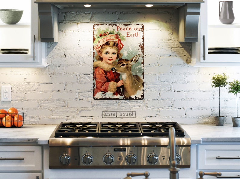 Puede incluir: Un letrero de metal de estilo vintage con una ni&ntilde;a y un ciervo. El letrero tiene un aspecto desgastado y dice "Peace on Earth".
