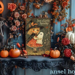 May include: A Halloween-themed display featuring a vintage-style illustration of a girl in a witch hat holding a ghost, with the text "Just a Little Spooky." The scene includes pumpkins, flowers, and a skeleton.