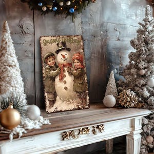 May include: A vintage-style metal sign with a snowman and two children. The sign reads "Seasons Greetings". The sign is surrounded by a white Christmas tree, a white flocked tree, and gold and white ornaments.