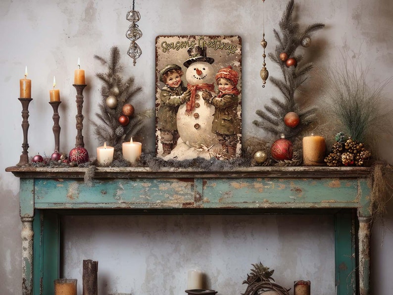 May include: Vintage Christmas metal sign featuring two children building a snowman. The sign has a rustic, distressed look and says 'Seasons Greetings'.  It's surrounded by candles, ornaments, and winter greenery on a rustic teal console table. The overall color palette is muted with browns, greens, and reds.