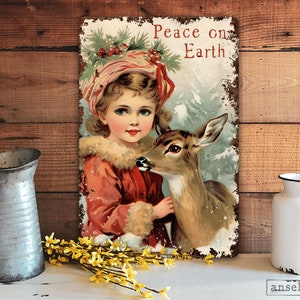 Puede incluir: Un letrero de metal de estilo vintage con una ni&ntilde;a con un vestido rojo sosteniendo un cervatillo. El letrero tiene un aspecto desgastado y dice "Peace on Earth".