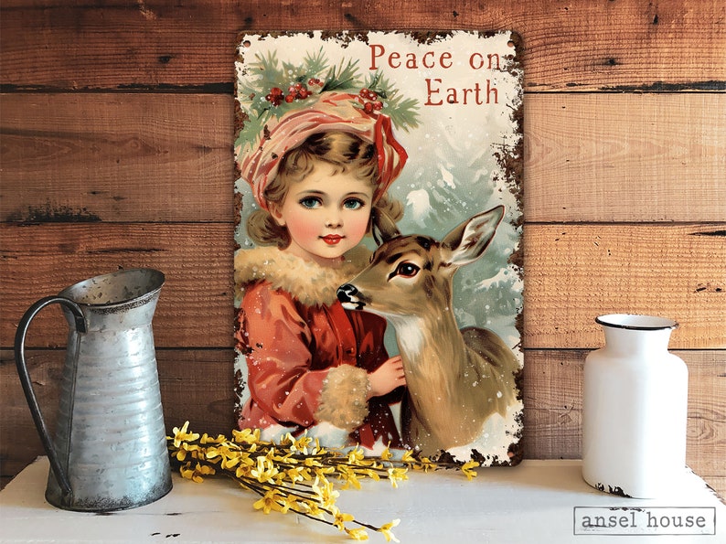 Puede incluir: Un letrero de metal de estilo vintage con una ni&ntilde;a con un vestido rojo sosteniendo un cervatillo. El letrero tiene un aspecto desgastado y dice "Peace on Earth".