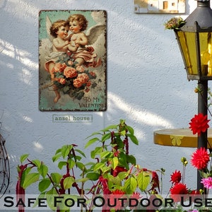 May include: A vintage metal sign with a faded, distressed look featuring two cherubs with wings holding a bouquet of pink roses. The sign has the text "To My Valentine" and the words "ansel house" at the bottom.