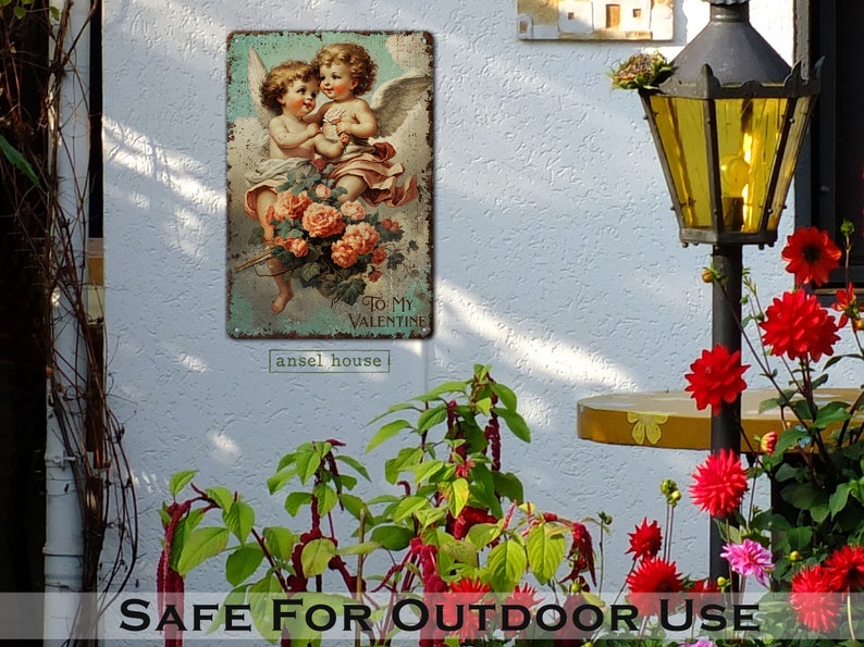 May include: A vintage metal sign with a faded, distressed look featuring two cherubs with wings holding a bouquet of pink roses. The sign has the text "To My Valentine" and the words "ansel house" at the bottom.