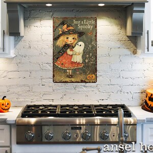May include: A vintage-style metal sign featuring a young girl dressed as a witch holding a ghost, with the text "Just a Little Spooky." The sign has a distressed finish and is mounted on a white brick wall.