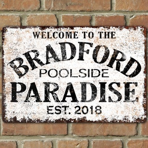 May include: White metal sign with black text that reads "Welcome to the Bradford Poolside Paradise Est. 2018". The sign has a distressed, vintage look.