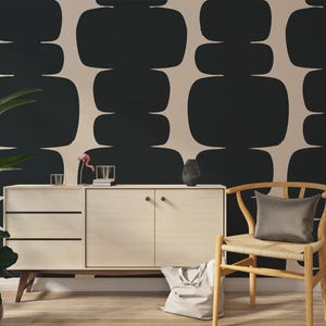 Peut inclure: Un mur beige avec un motif abstrait noir et blanc. Une chaise en bois avec un si&egrave;ge en osier et un coussin gris est plac&eacute;e devant un meuble en bois clair avec deux tiroirs et deux portes.