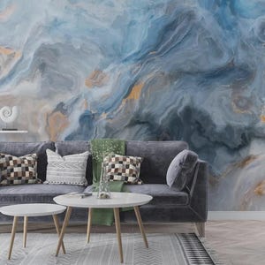 May include: A modern living room with a grey sofa, patterned cushions, and a white coffee table. The wall is decorated with a large abstract mural in blue, grey, and gold tones, creating a stylish and contemporary atmosphere.