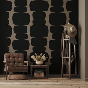 Peut inclure: Un int&eacute;rieur de salon avec un fauteuil en cuir marron, une petite table d'appoint en bois avec un panier en osier et un porte-manteau en bois avec un chapeau de paille et une &eacute;charpe. Le mur est recouvert d'un papier peint avec un motif g&eacute;om&eacute;trique de formes arrondies noires et brunes.