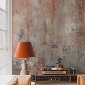 May include: An orange table lamp with a beige base sits in front of a textured wall with shades of gray, orange, and white. A wooden record player and small potted plant are on a wooden cabinet.