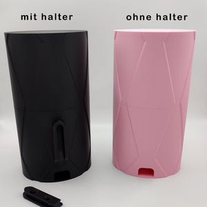 May include: Two wall mounts, one black and one pink, with a geometric pattern. The black wall mount has a holder attached to it. The pink wall mount does not have a holder. The text "Wandhalterung" is at the top of the image. The text "mit halter" is below the black wall mount. The text "ohne halter" is below the pink wall mount.