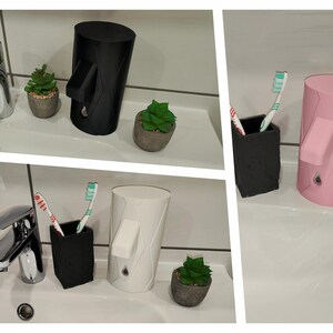 May include: Three bathroom countertop soap dispensers in black, white and pink. Each dispenser has a pump and a round, cylindrical shape. The dispensers are on a white countertop with a sink and faucet in the background.