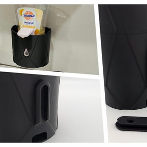 May include: A black plastic soap dispenser with a diamond pattern. The dispenser has a small opening on the side for mounting. The dispenser is mounted on a white tiled wall. The dispenser is holding a bottle of hand soap.