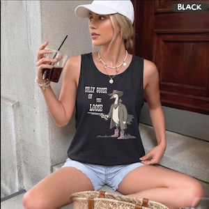 May include: A black sleeveless tank top featuring a graphic print of a goose wearing a cowboy hat, a trench coat, and pink boots, holding a revolver. The text "SILLY GOOSE ON THE LOOSE" is printed in white above the goose illustration.