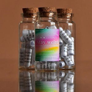 Puede incluir: Tres frascos de vidrio llenos de trozos de papel enrollados. Los frascos tienen tapones de corcho y etiquetas que dicen "Poesía medicinal hecha a mano", "Mantente raro", "Por a RiverIris", y "Los efectos secundarios pueden incluir: Paradoja, Caos, Maravilla".