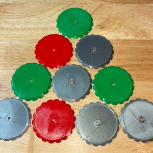 Könnte beinhalten: Neun runde, plastische Scheiben mit gewellten Kanten. Die Scheiben sind in drei Farben: rot, grün und grau. Die grauen Scheiben haben eine strukturierte Oberfläche.