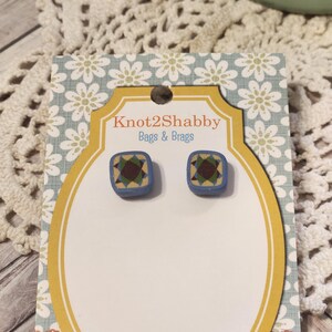 May include: A pair of square stud earrings with a blue border and a geometric design in the center. The earrings are displayed on a card with the text "Knot2Shabby Bags & Brags". The card has a floral pattern.