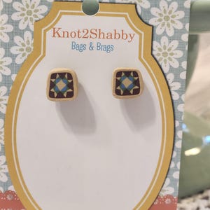 May include: A pair of square stud earrings with a quilt block design. The earrings are displayed on a decorative card with the text "Knot2Shabby Bags & Brags". The earrings feature a geometric pattern in shades of blue, brown, and burgundy.