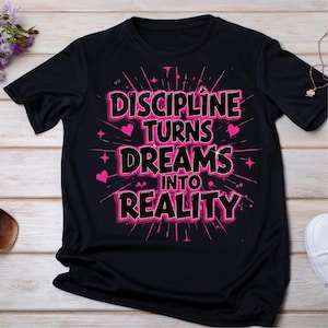 May include: Black t-shirt with the text "DISCIPLINE TURNS DREAMS INTO REALITY" in a pink and black design. The design includes pink hearts and starbursts. The shirt is made of a soft, dark fabric.