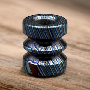 May include: A multi-layered, cylindrical bead with a blue and silver striped pattern. The bead has a hole through the center and is made of a metallic material. The bead is a decorative item.