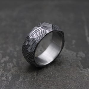 Könnte beinhalten: Ein silberner Ring mit geometrischem, facettiertem Design. Der Ring ist aus strukturiertem Metall mit einer gehämmerten Oberfläche.